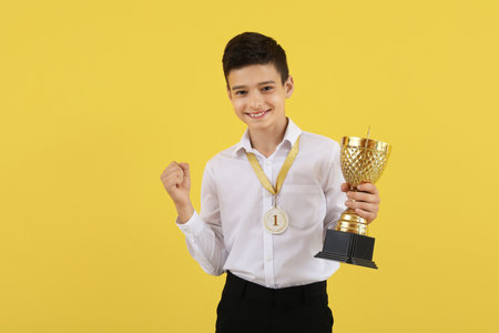 Smart little school boy with prize cup and medal on yellow backgroundの写真素材