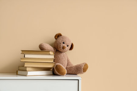 Stack of books with toy bear on chest of drawers near beige wallの写真素材