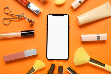 Composition with modern mobile phone, different cosmetics and makeup accessories on color backgroundの写真素材