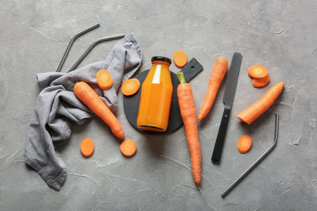 Board with bottle of fresh carrot juice on gray tableの写真素材