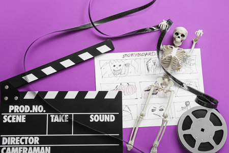 Clapperboard with film reel, storyboard and skeleton on purple background. Halloween celebrationの写真素材