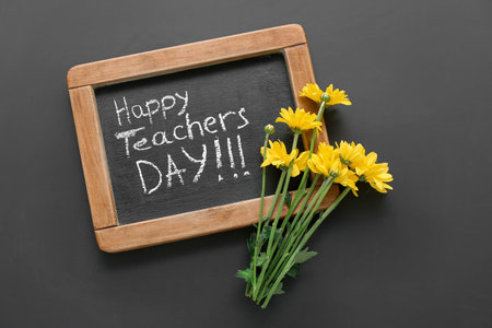 Blackboard with text HAPPY TEACHER'S DAY and beautiful flowers on black backgroundの写真素材