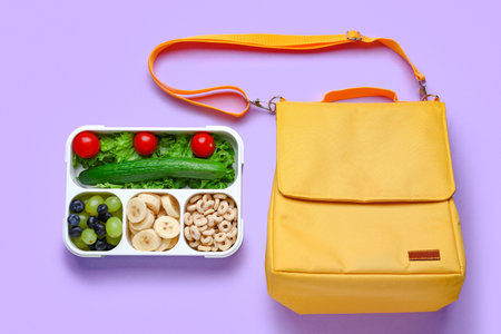Bag and lunchbox with tasty food on lilac backgroundの写真素材