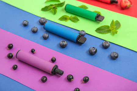 Electronic cigarettes with berries and mint on colorful background