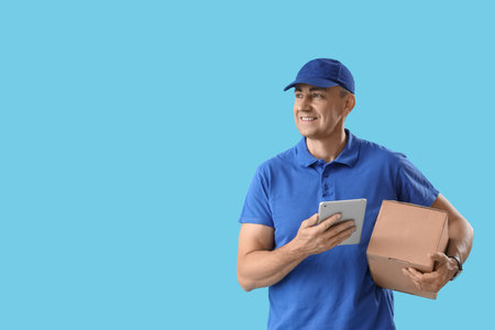 Mature courier with tablet computer and parcel on blue backgroundの写真素材
