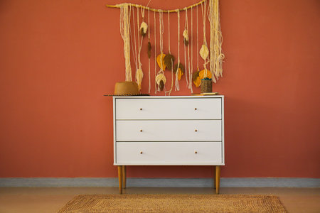 Stylish straw hat and houseplant on chest of drawers near color wallの写真素材