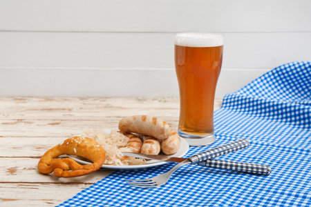 Plate with tasty Bavarian sausages, pretzel, sauerkraut and glass of beer on white wooden backgroundの写真素材