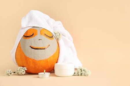 Pumpkin with clay mask, towel, cream and burning candle on beige backgroundの写真素材
