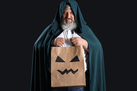 Mature man dressed for Halloween with gift bag on black backgroundの写真素材