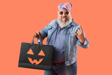 Mature biker with Halloween gift bag showing "devil horns" on color backgroundの写真素材