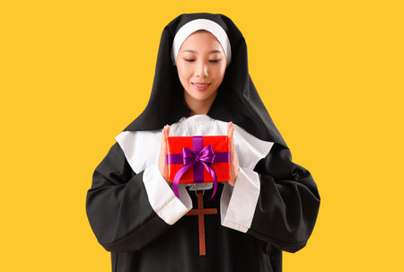 Young Asian woman dressed as nun with Halloween gift on yellow backgroundの写真素材
