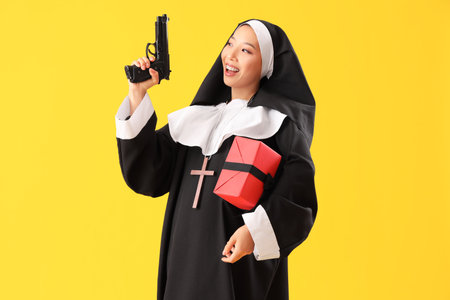 Young Asian woman dressed as nun with gun and Halloween gift on yellow backgroundの写真素材