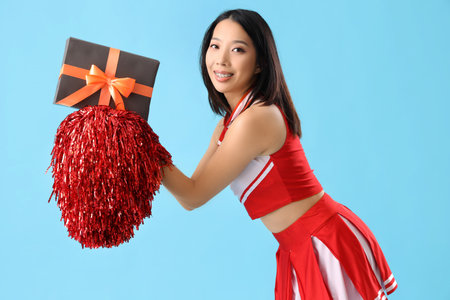 Young Asian cheerleader with Halloween gift on blue backgroundの写真素材