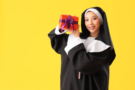 Young Asian woman dressed as nun with Halloween gift on yellow backgroundの写真素材