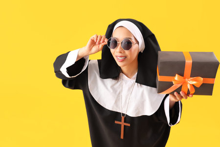 Young Asian woman dressed as nun with Halloween gift on yellow backgroundの写真素材