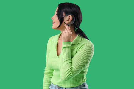 Young woman magnifying her ear on green backgroundの写真素材