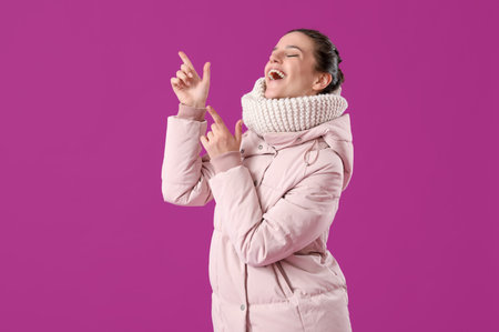 Young woman in down coat pointing at something on purple backgroundの写真素材