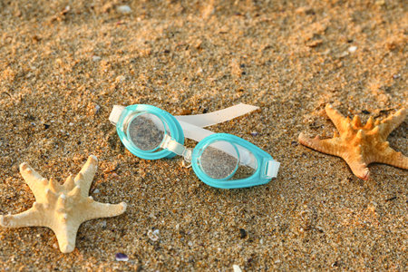 New swimming goggles and starfishes on sandの写真素材