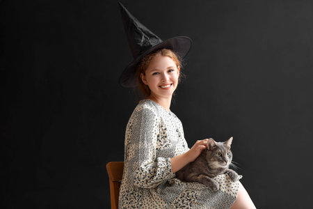 Young woman in witch hat with cute cat sitting at home