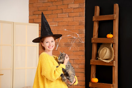 Young woman in witch hat with cute cat at homeの写真素材