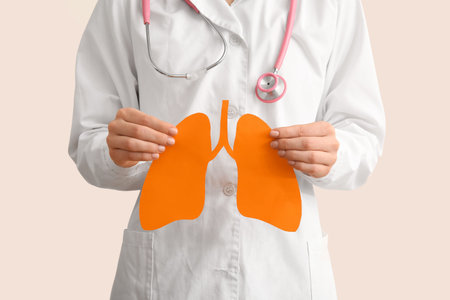 Doctor holding orange paper lungs on light background. Cancer concept