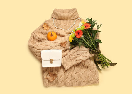 Beautiful autumn composition with stylish sweater, leaves, pumpkin and bouquet of flowers on beige backgroundの写真素材