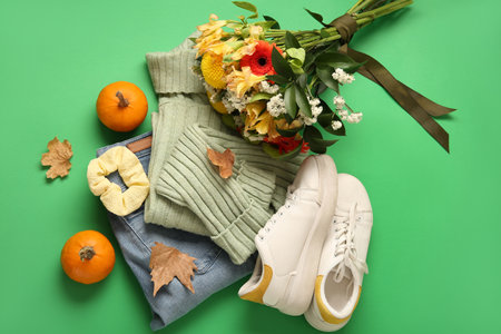 Beautiful autumn composition with stylish clothes, leaves, pumpkins and bouquet of flowers on green backgroundの写真素材