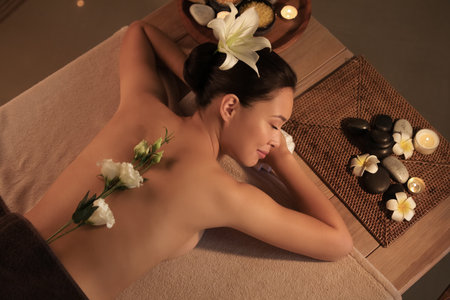 Young woman with flowers lying in dark spa salon, top viewの写真素材