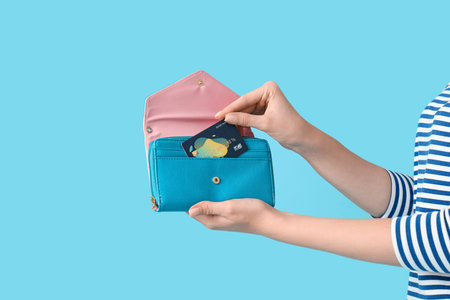 Young woman with credit card and wallet on blue background, closeup