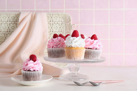 Stand and plate with tasty raspberry cupcakes on tableの写真素材