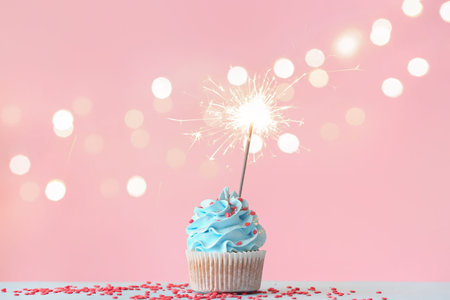Tasty birthday cupcake with sparkler on color backgroundの写真素材
