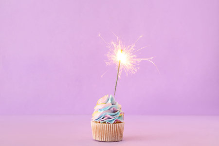 Tasty birthday cupcake with sparkler on purple backgroundの写真素材