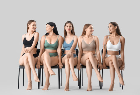 Many beautiful women in underwear sitting on chairs against light backgroundの写真素材