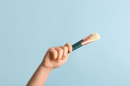 Female hand with makeup brushes on blue background