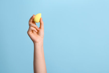 Female hand with yellow makeup sponge on blue backgroundの写真素材