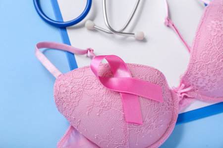 Bra with awareness ribbon, stethoscope and clipboard on blue background, closeup. Breast cancer conceptの写真素材