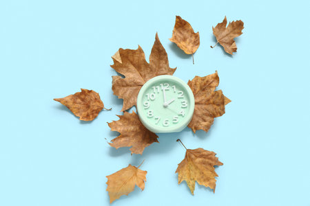 Alarm clock with fallen leaves on blue backgroundの写真素材