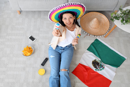 Young Mexican woman in sombrero hat with maracas sitting at homeの写真素材
