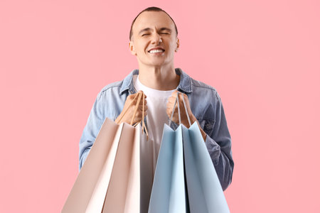 Young man with shopping bags on pink background