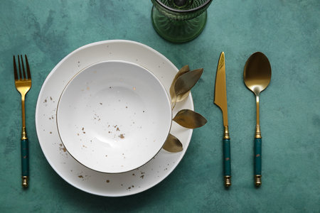 Elegant table setting with golden leaves and cutlery on green table
