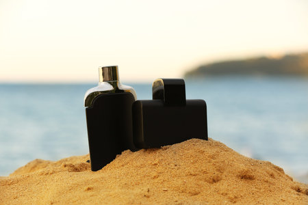 Bottles of luxury perfume on beach sand near ocean