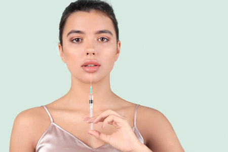 Young woman with beautiful lips and syringe on green background, closeupの写真素材