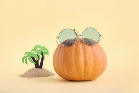 Halloween pumpkin with stylish sunglasses and beach decor on beige backgroundの写真素材