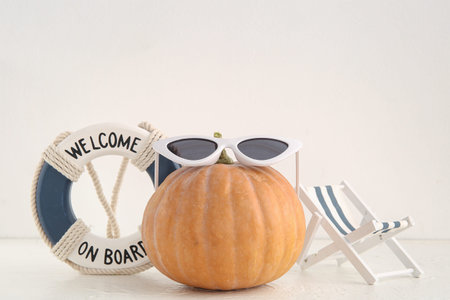 Halloween pumpkin with stylish sunglasses, beach deck chair and lifebuoy ring on light background