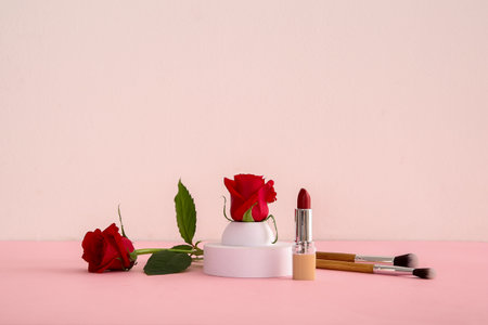 Composition with makeup brushes, lipstick and beautiful red rose flowers on color backgroundの写真素材