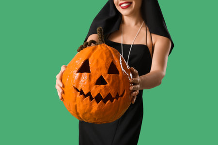 Young woman dressed for Halloween as nun with pumpkin on green background, closeupの写真素材