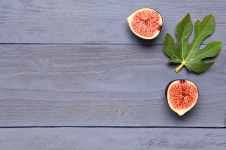 Halves of fresh ripe fig and leaf on blue wooden background