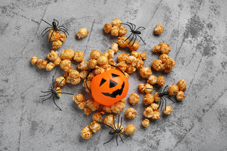 Caramel popcorn with Halloween pumpkin and spiders on gray grunge backgroundの写真素材
