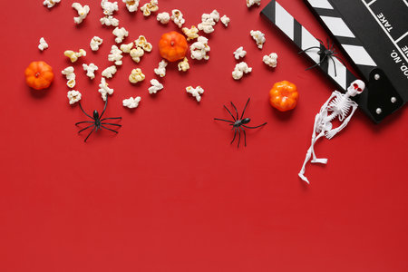 Composition with tasty popcorn, clapperboard, skeleton and pumpkins for Halloween celebration on red backgroundの写真素材
