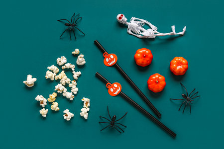Composition with tasty popcorn, straws, spiders and skeleton for Halloween celebration on green backgroundの写真素材